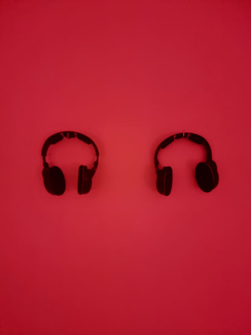 Two pairs of black headphones facing each other on a flat red background.