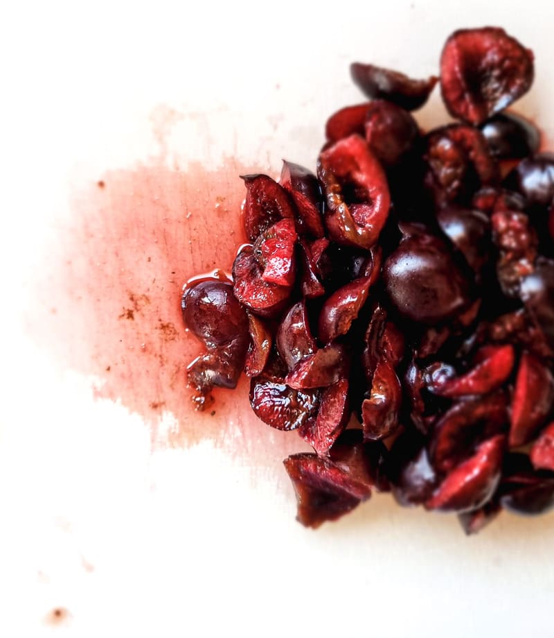Pitted cherries piled on a white surface, stained with red juice.