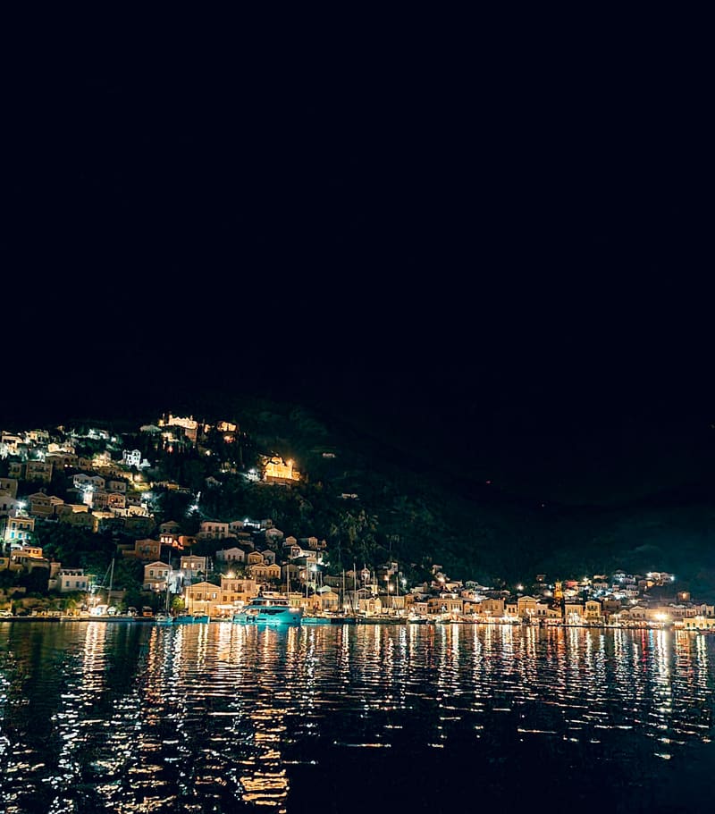 A hillside town lit up at night, its lights reflected in the harbour.