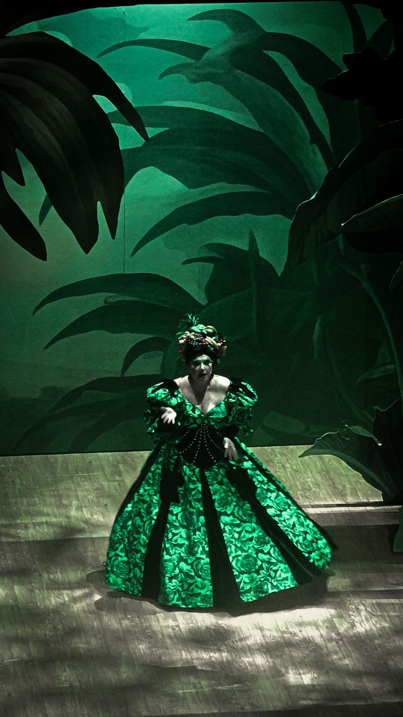 A woman in a sequined green gown posing in front of painted leaves.