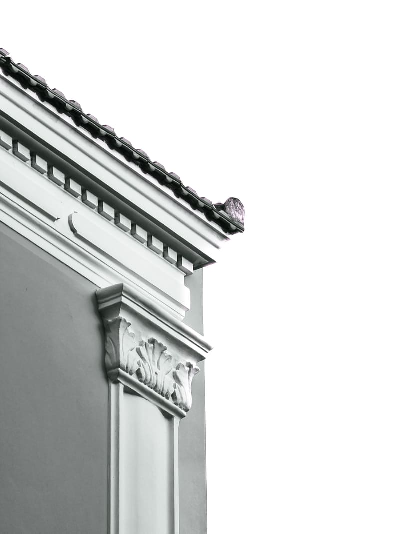 Black and white: the corner of a neoclassical building, its cornice and carved pilaster against a white sky.
