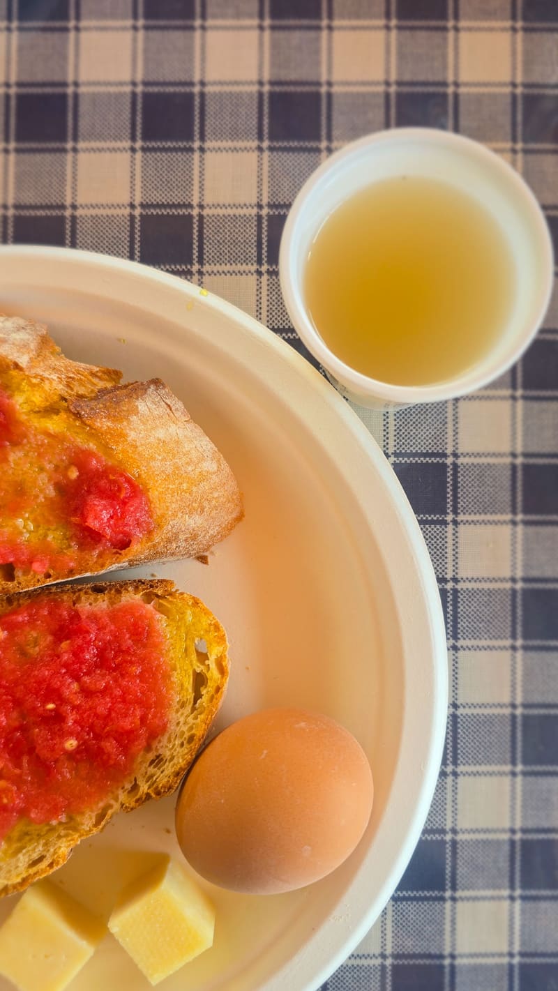 Breakfast on a checked tablecloth: tomato toast, cheese, an egg and a cup of juice.