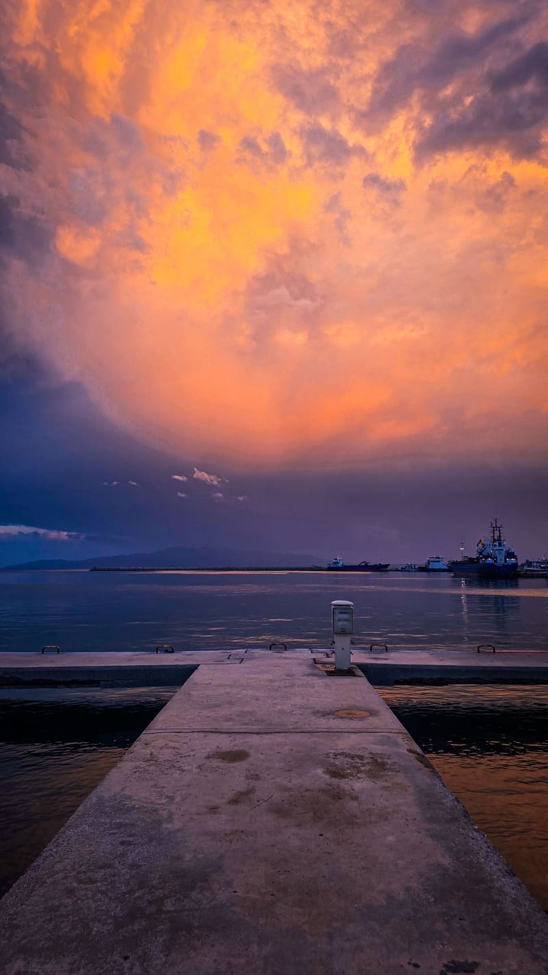 Orange storm clouds over a jetty and still water.