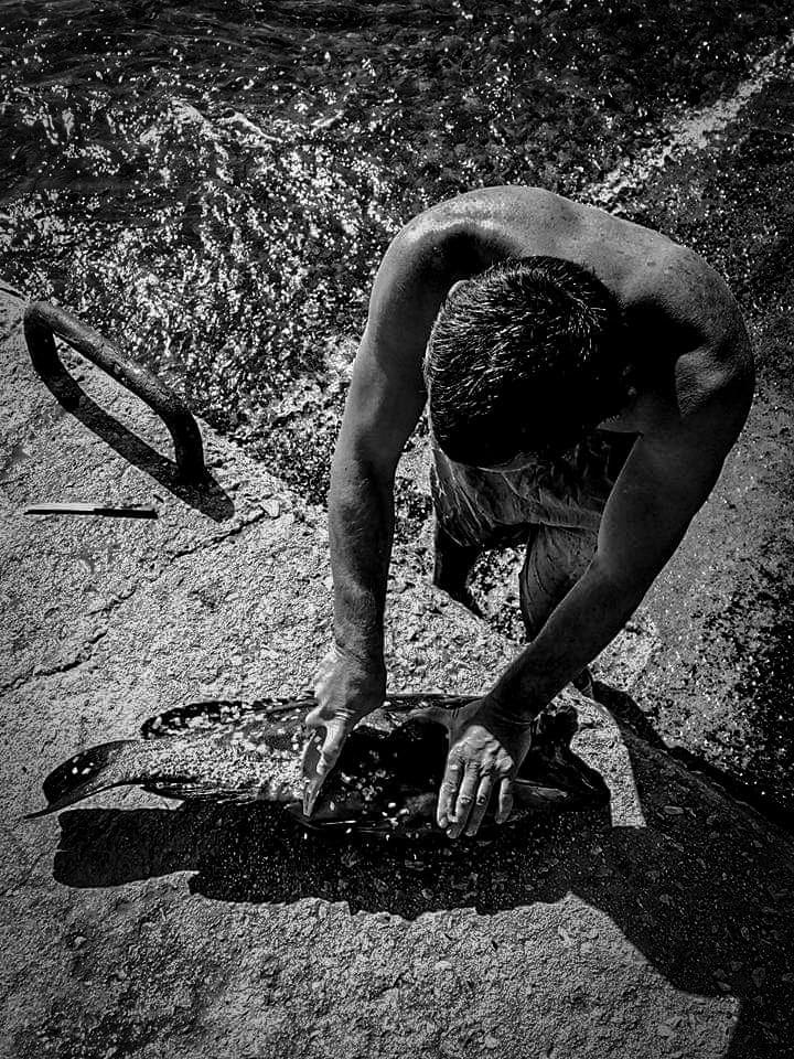 Black and white: a man crouched over textured rock, lit from above.