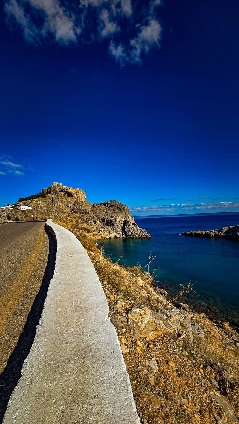 A coastal path curving along the rocks above a blue bay.