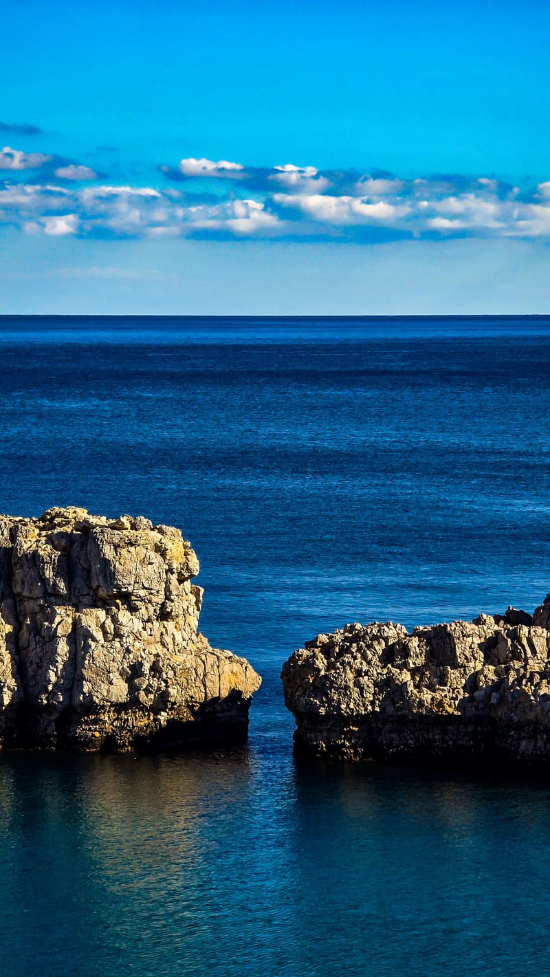 Two rocks in a deep blue sea under a strip of clouds.
