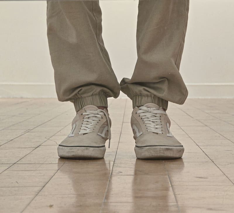 Grey trousers and canvas sneakers standing on a reflective tiled floor.