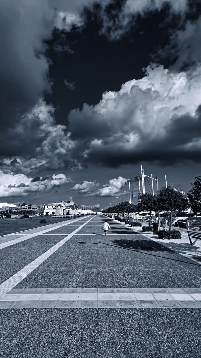 Black and white: a wide harbour promenade under heavy clouds.