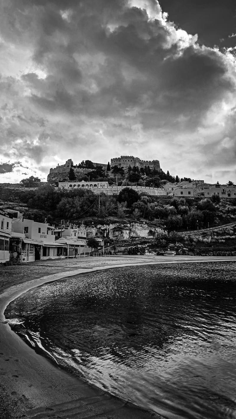 Black and white: a curved shoreline below a hilltop castle and village.