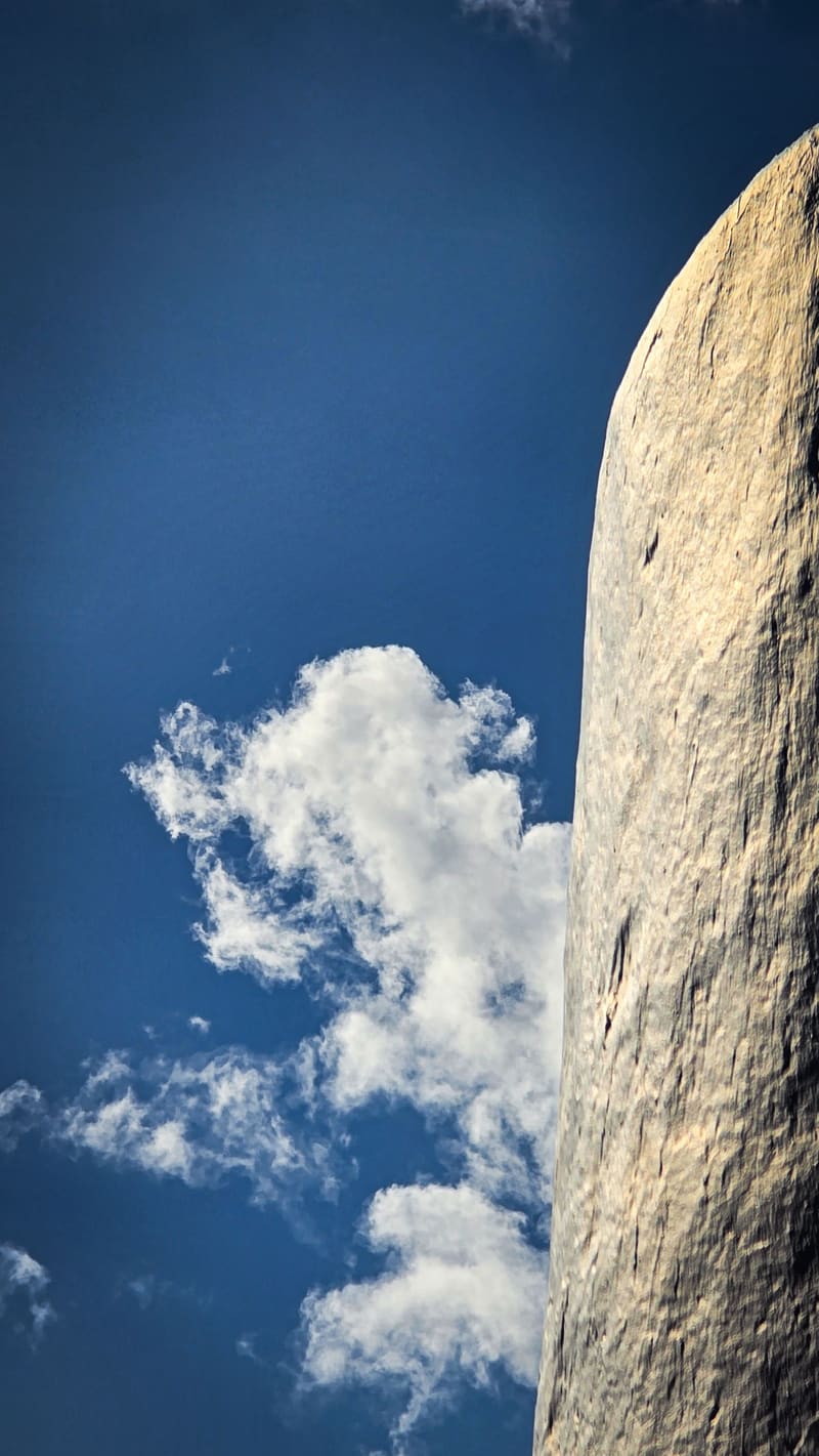 The curved edge of a white stone tower against a deep blue sky with clouds.