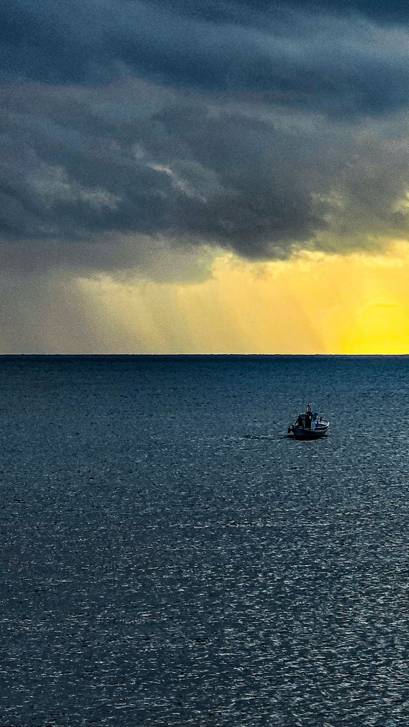 A small boat on a dark sea under a stormy sky with a band of yellow light.
