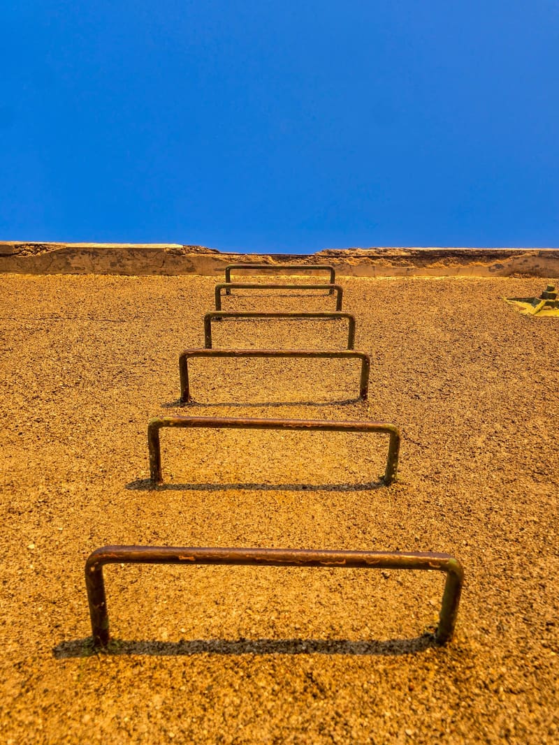 Metal rungs set into a sandy slope, climbing towards a deep blue sky.