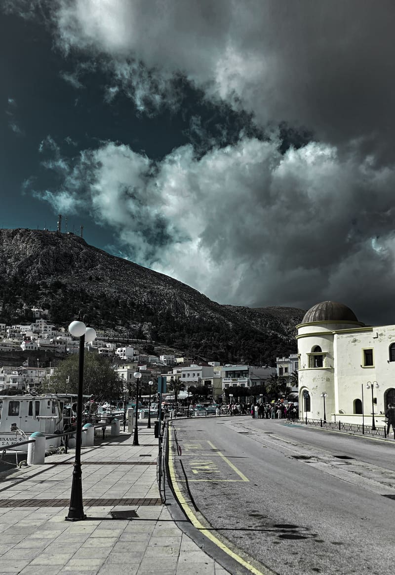 A seaside street with a domed white building under stormy clouds.
