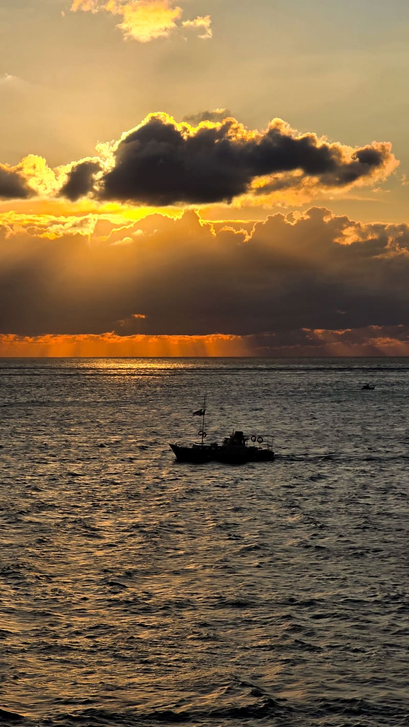 A small boat silhouetted on the sea beneath a golden sunset cloud.