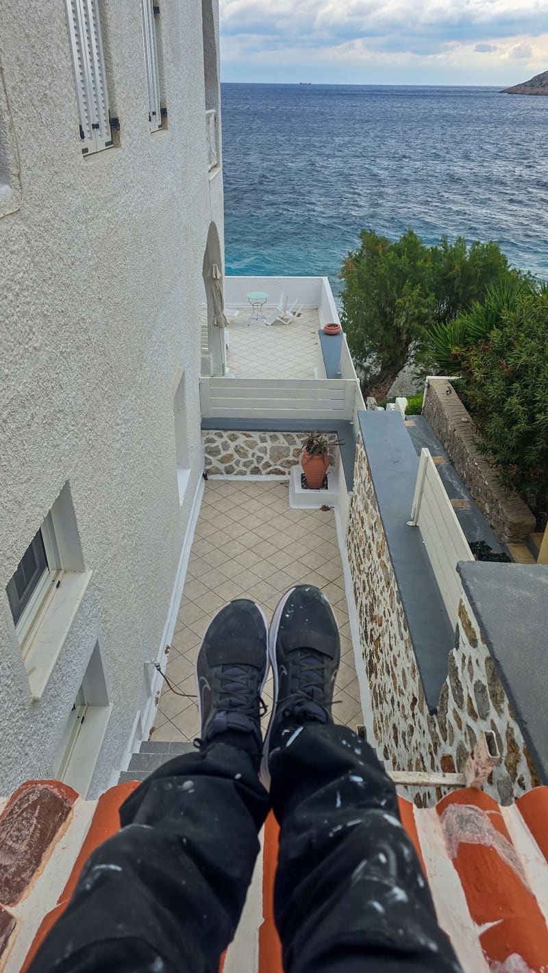 Legs stretched out on a balcony, looking down a white building towards the sea.