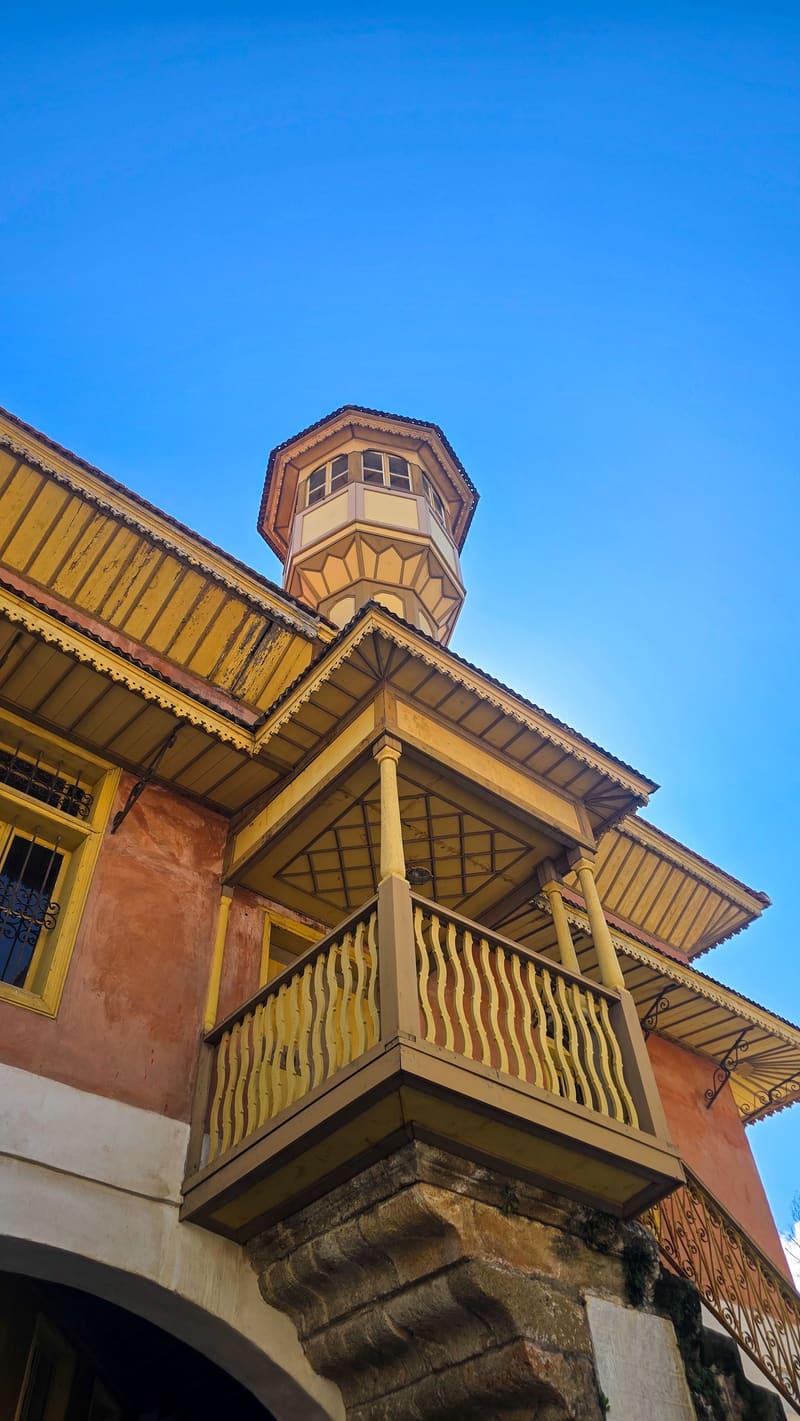 Looking up at a wooden balcony and tower on an ochre building.