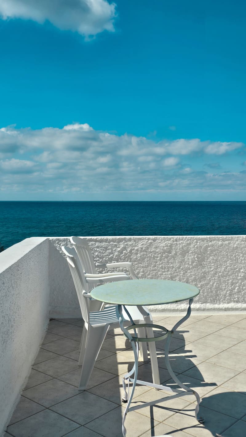 A balcony table and chair facing the sea.