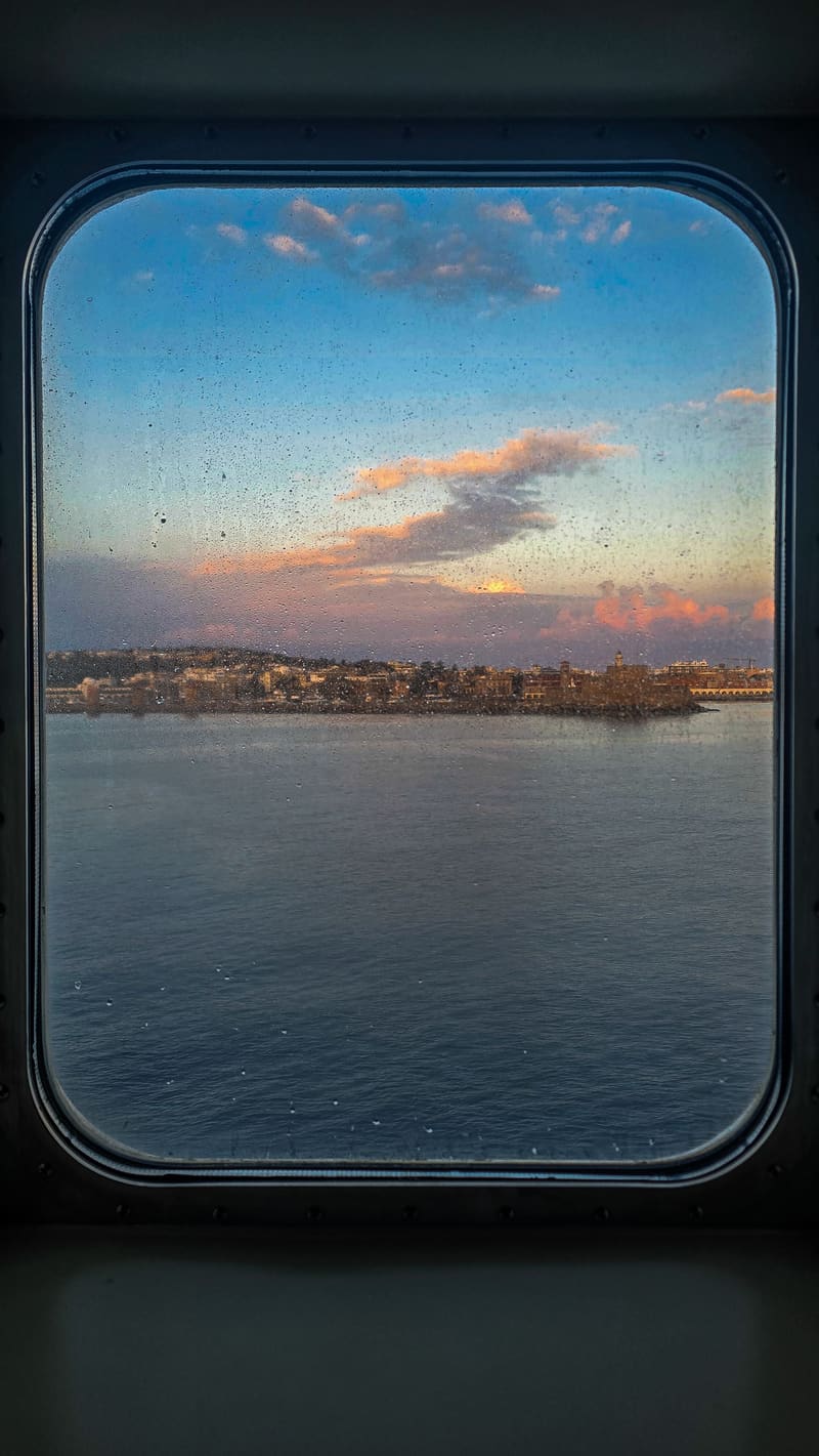 A ship's window framing a coastal town at sunset.