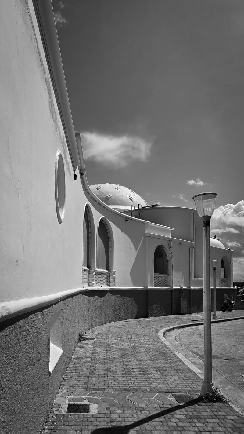 Black and white: a curving whitewashed street with a lamp post.