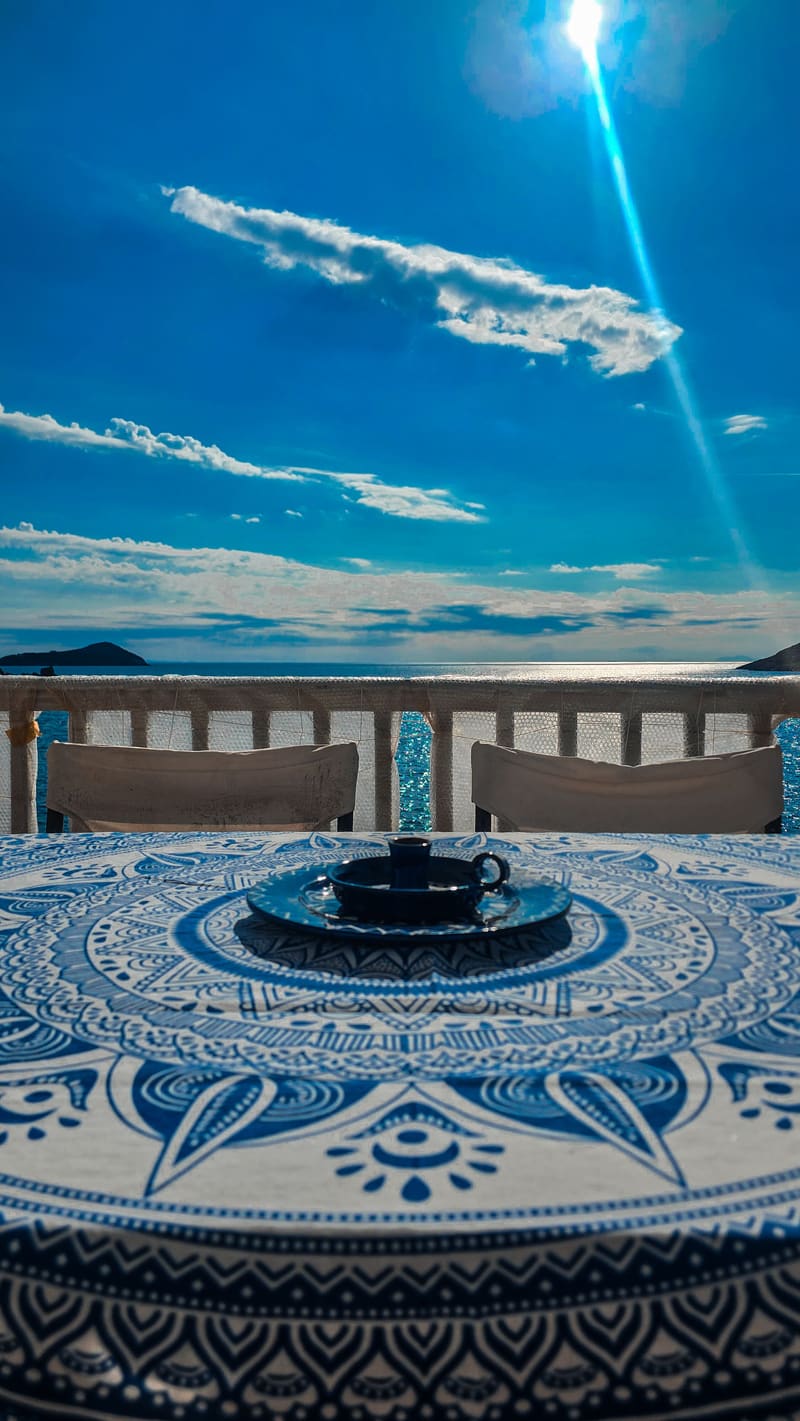 A mosaic-topped table on a terrace, sunlight over the sea.