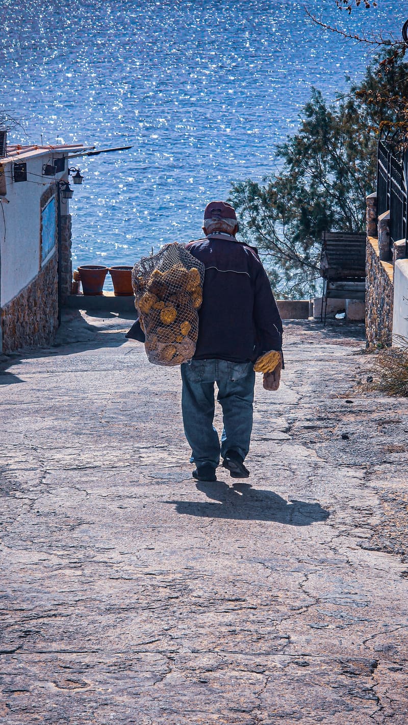 A man carrying a bag down a sunny stone path.