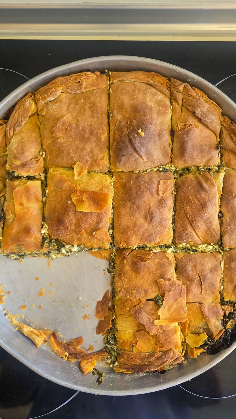 A golden spinach pie cut into squares in a round tray.
