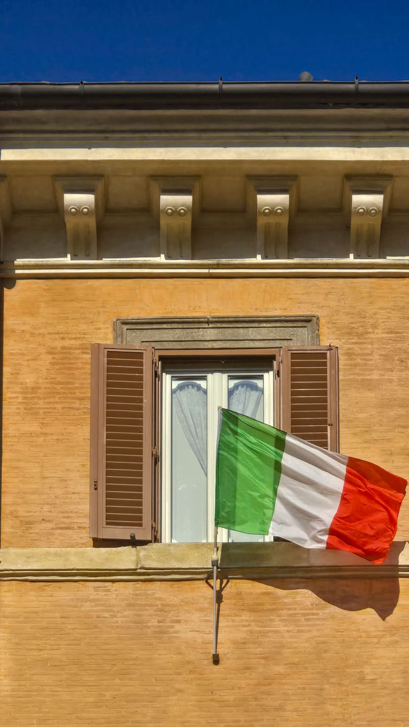 An Italian flag hanging from a window of an ochre building.