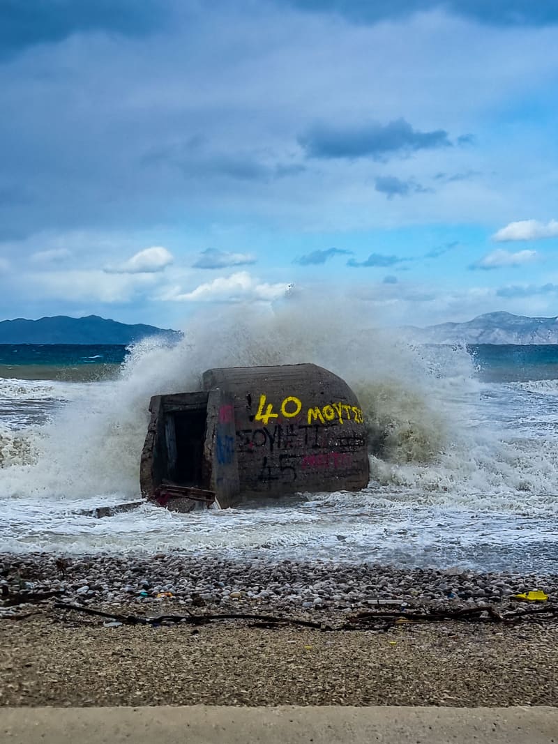 A wave breaking over a graffiti-covered concrete bunker on a beach.