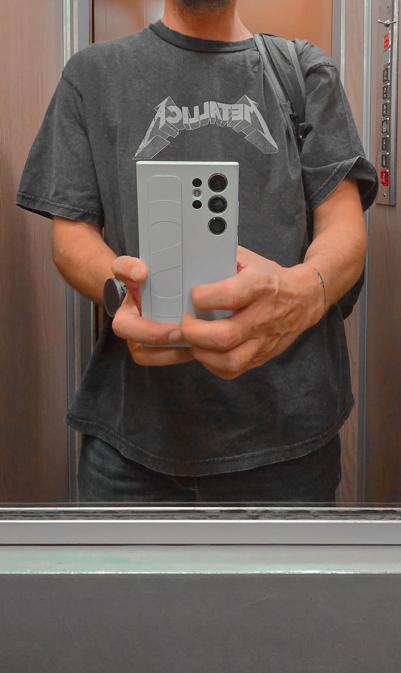A mirror selfie in a lift, phone held in front of a grey T-shirt.