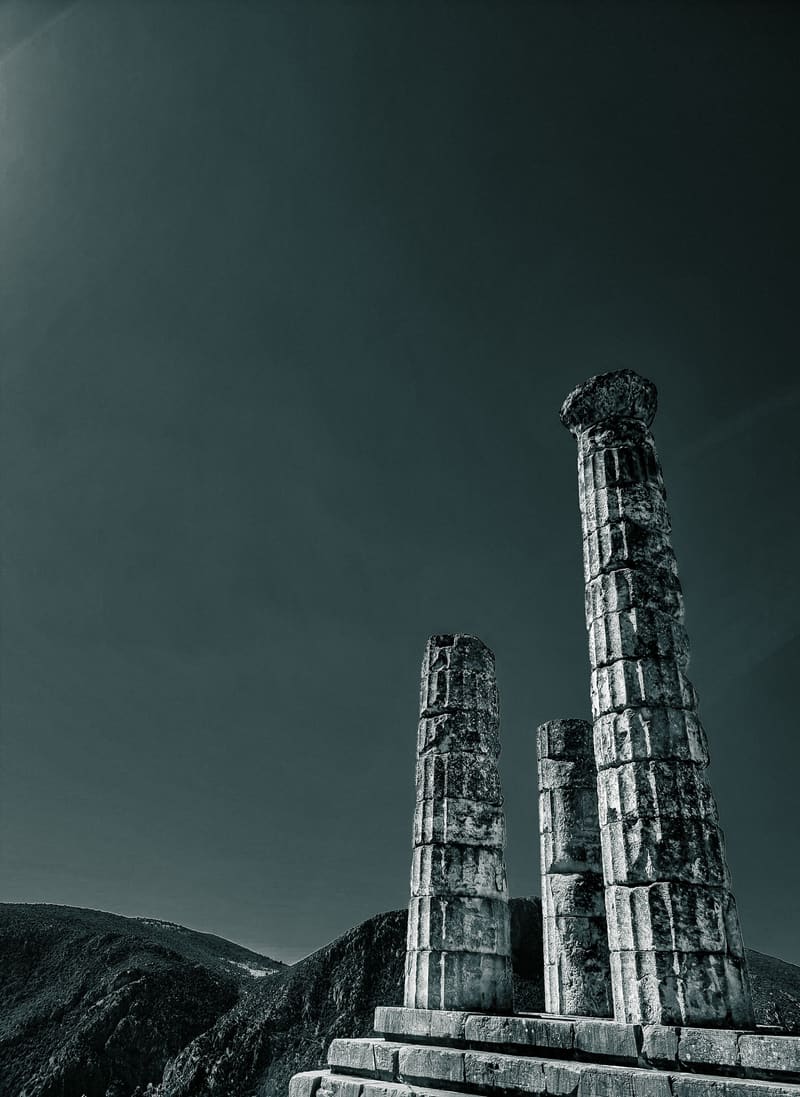 Two ancient columns rising from a stone base against a dark, moody sky.