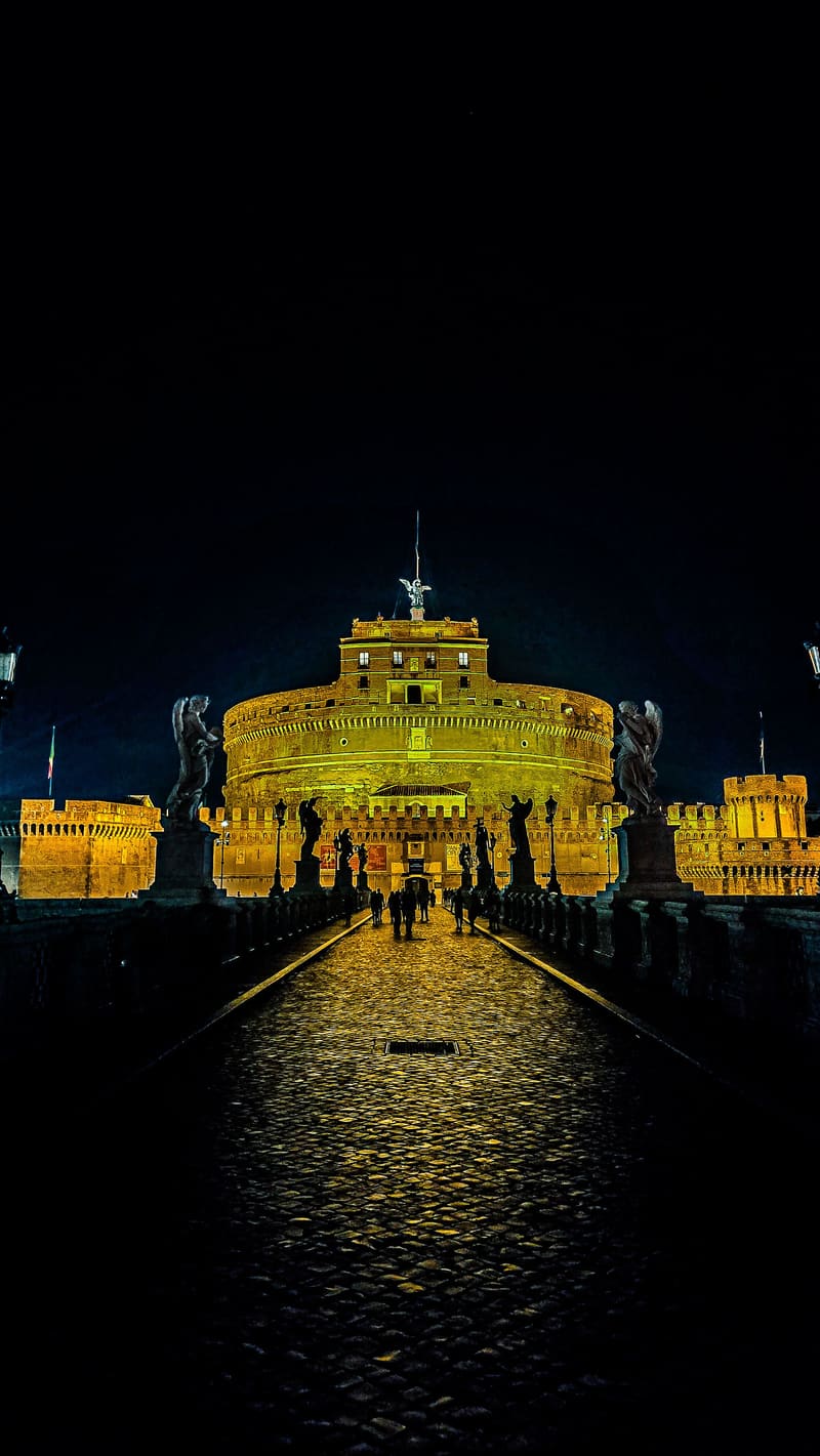 A floodlit castle reflected on a wet bridge at night.