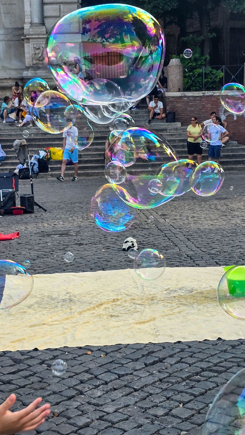 Giant soap bubbles floating over steps and a crowd.