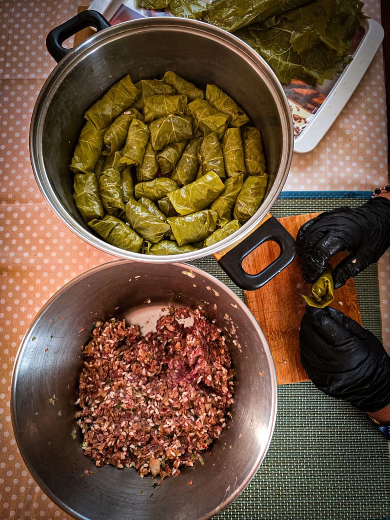 A pot of stuffed vine leaves and a bowl of minced filling, with gloved hands at work.