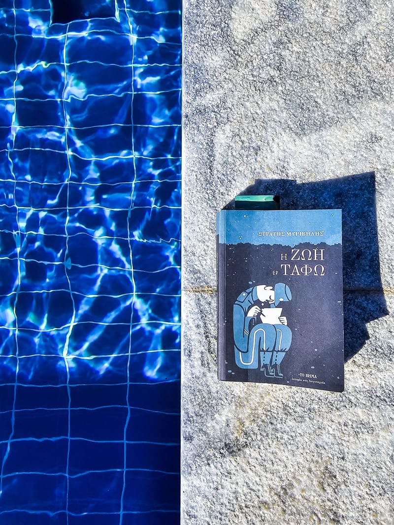 A book lying on a towel beside a rippling blue pool.