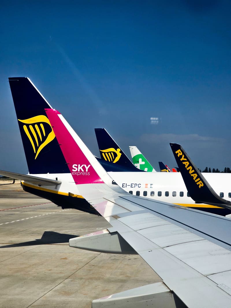 The tails of several airliners seen past an aircraft wing on the tarmac.