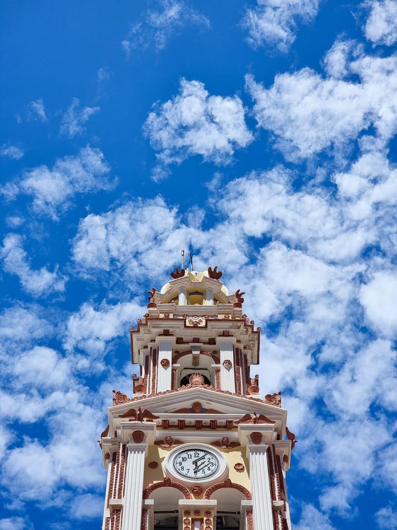 An ornate red and white clock tower rising into a blue sky full of small clouds.