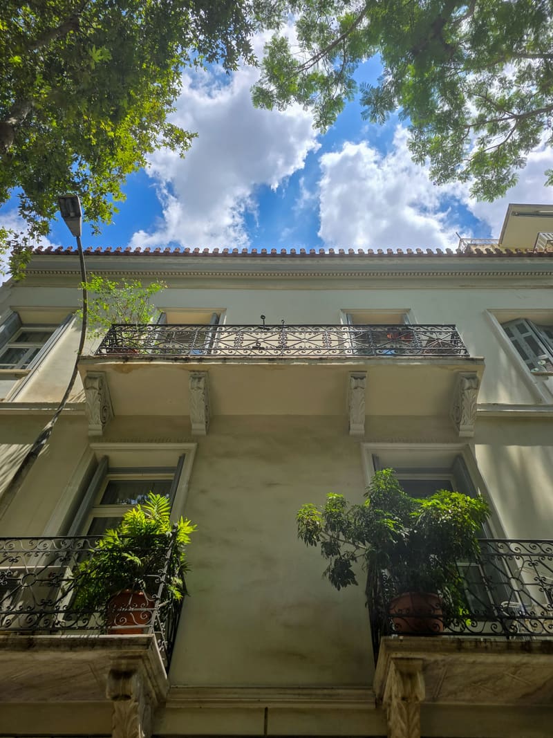 Looking up at the balconies of a neoclassical building through trees.