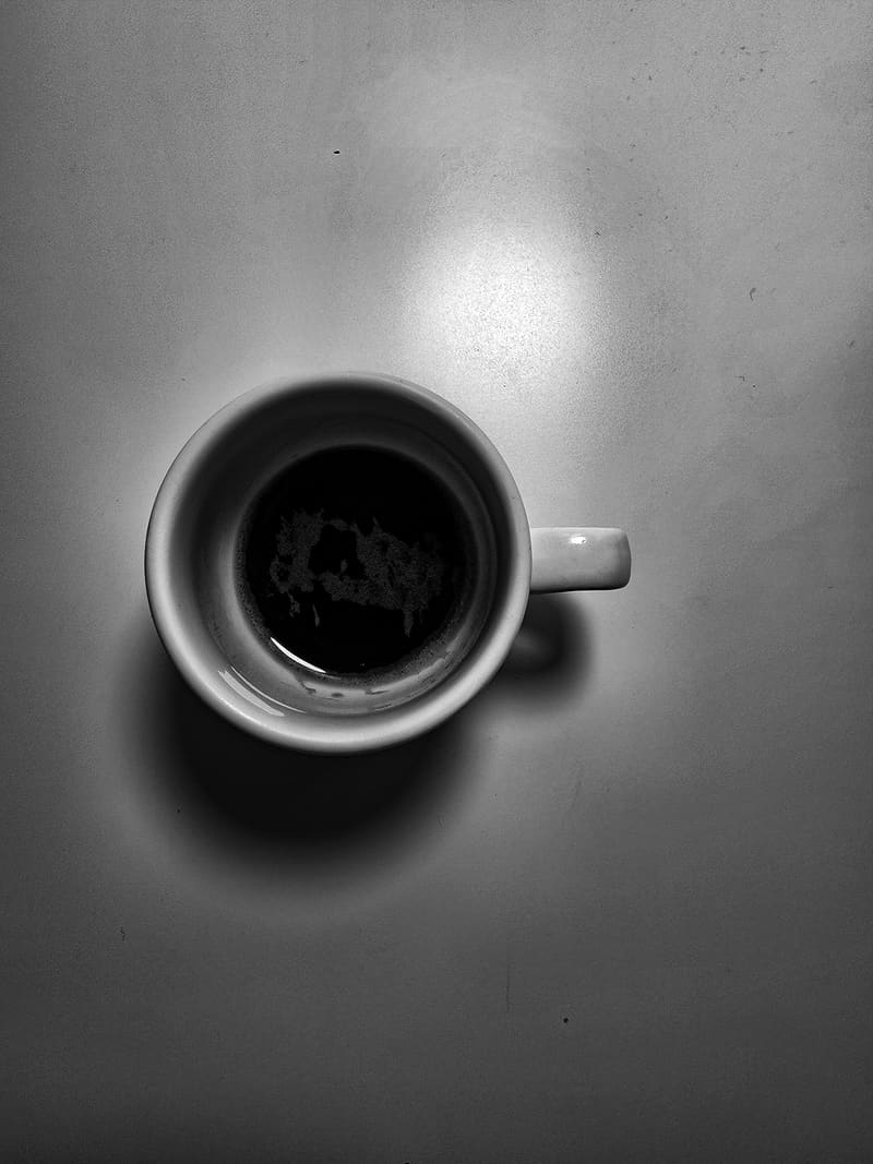 Black and white: a cup of black coffee seen from above on a grey surface, casting a soft shadow.