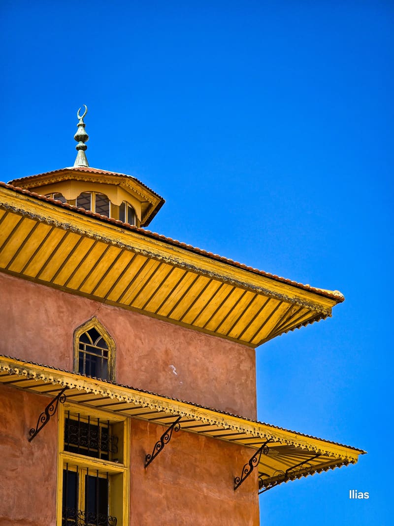 An ochre building with a yellow eave and a small dome against a blue sky.