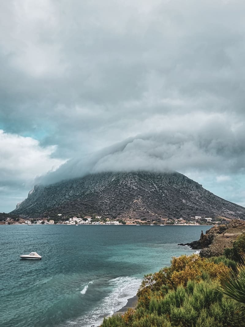 A mountainous island under low cloud, with a curving bay and a boat on grey-green water.