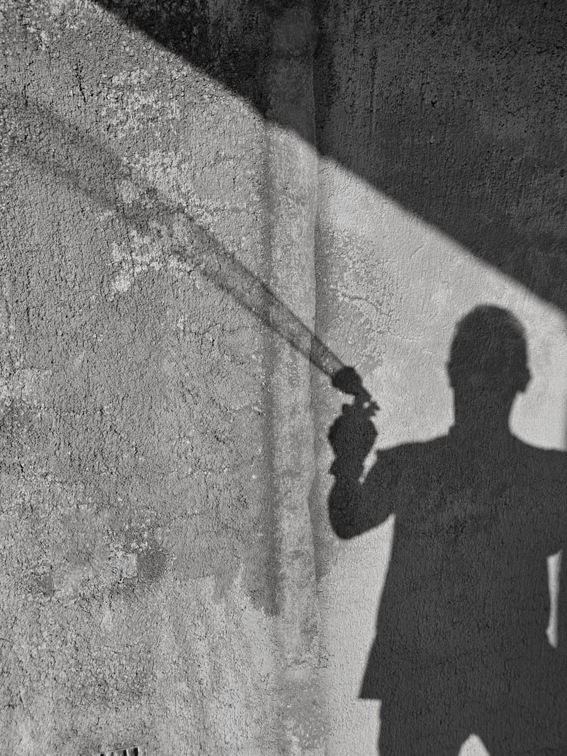 Black and white: the shadow of a person on a rough wall, crossed by a diagonal band of light.