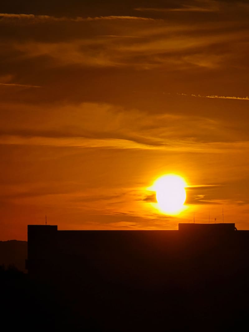 The sun setting orange behind the silhouette of a building.