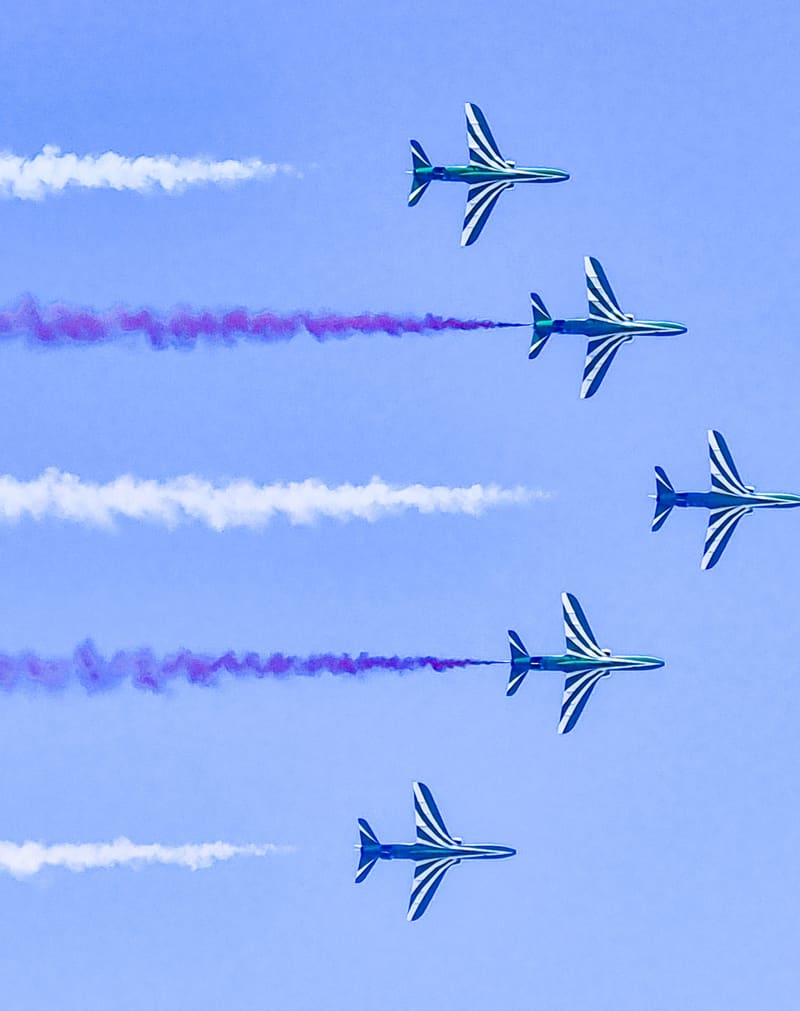Five jets flying in formation, trailing white and purple smoke across a blue sky.