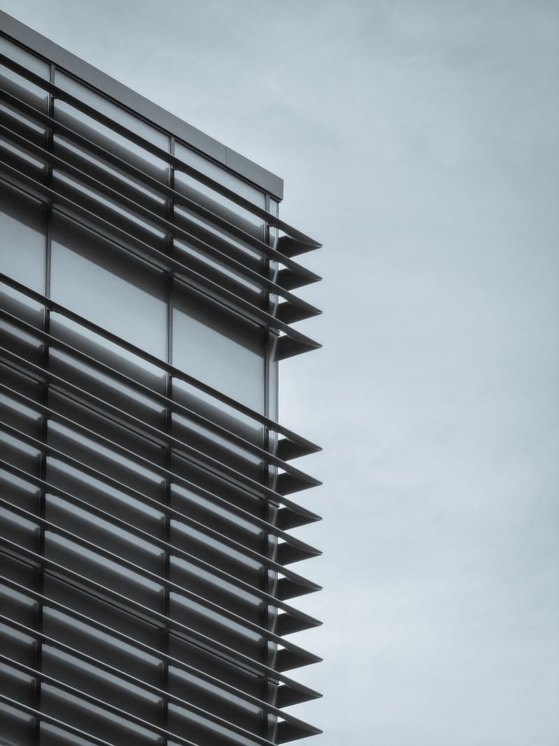 The corner of a modern building lined with dark horizontal louvres, against a pale sky.