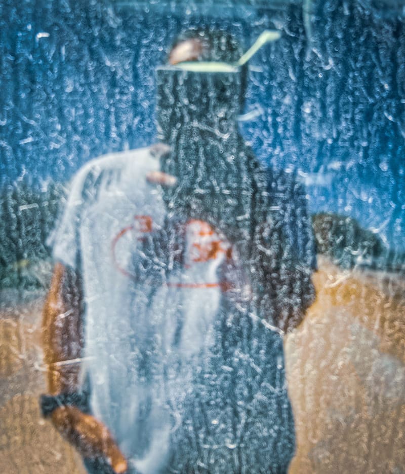 A figure seen through scratched, frosted glass.