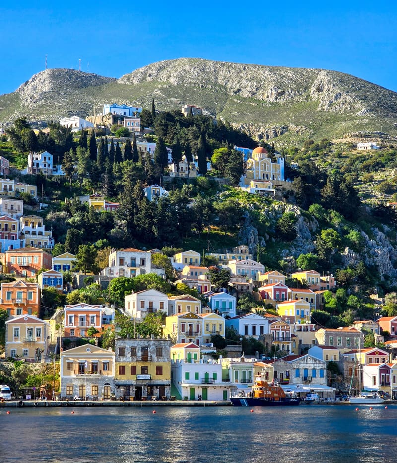 Colourful neoclassical houses stacked up a hillside above a harbour.