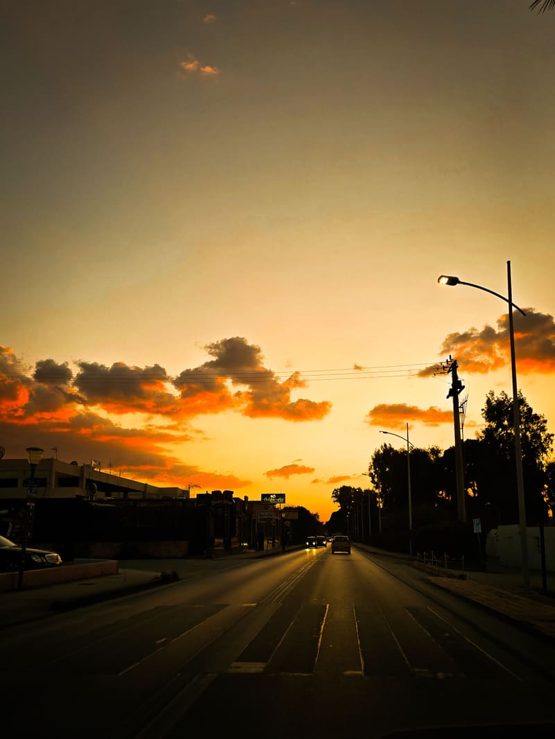Sunset over an empty road lined with street lamps.