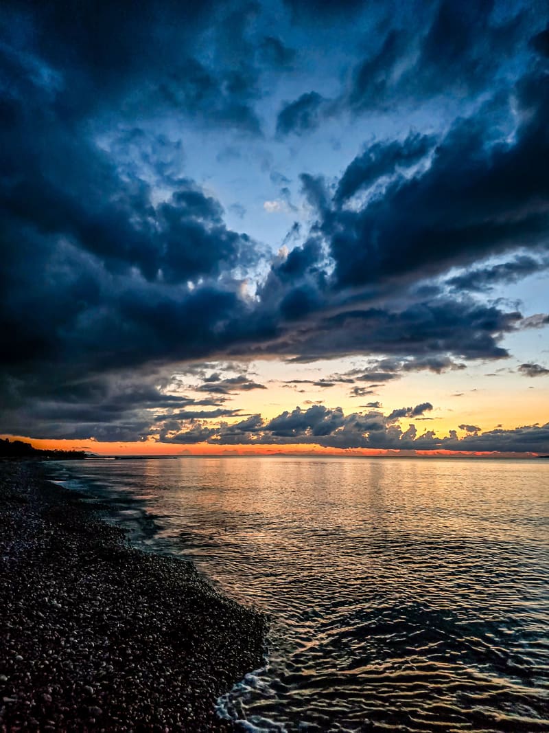 Dark storm clouds over a pebble beach at sunset.