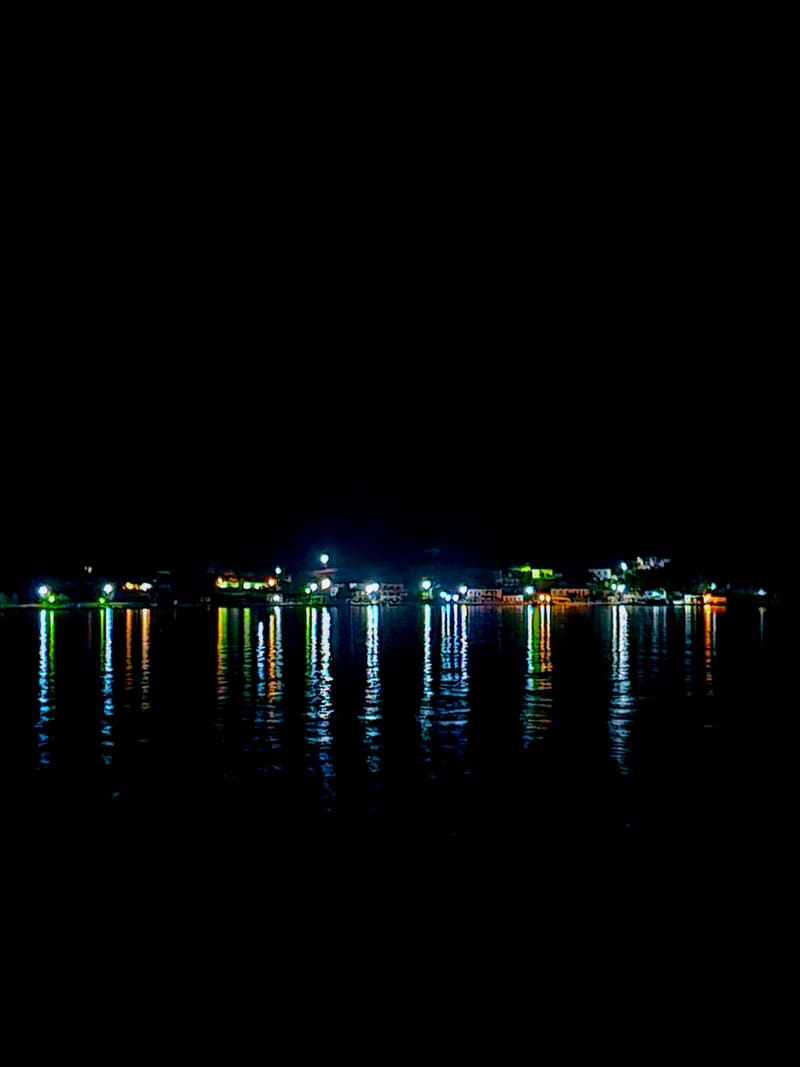 The lights of a coastline reflected in black water at night.