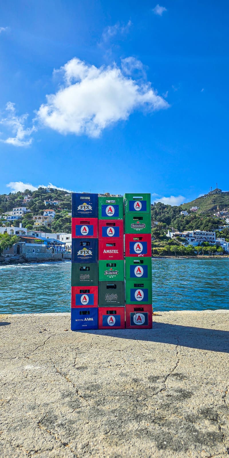 A stack of colourful crates on a quay, with hills and sea behind.